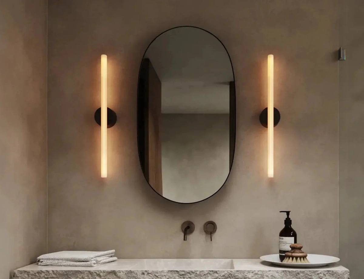 Oválne zrkadlo a dve svietidlá v kúpeľni so svetlými stenami